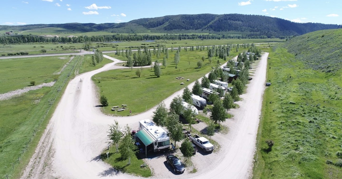 Aerial view of Eagle Soaring RV Park in summer, showing green pull-through sites, rows of aspen trees, and forested foothills near Steamboat Springs